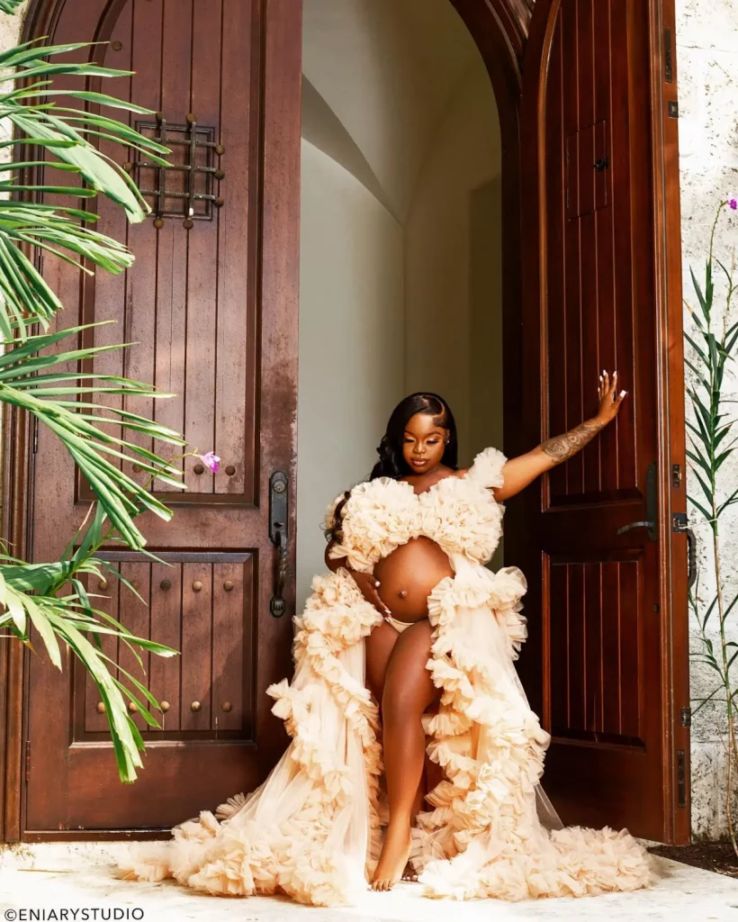 Maternity portrait in a feathered couture robe framed by wooden doors