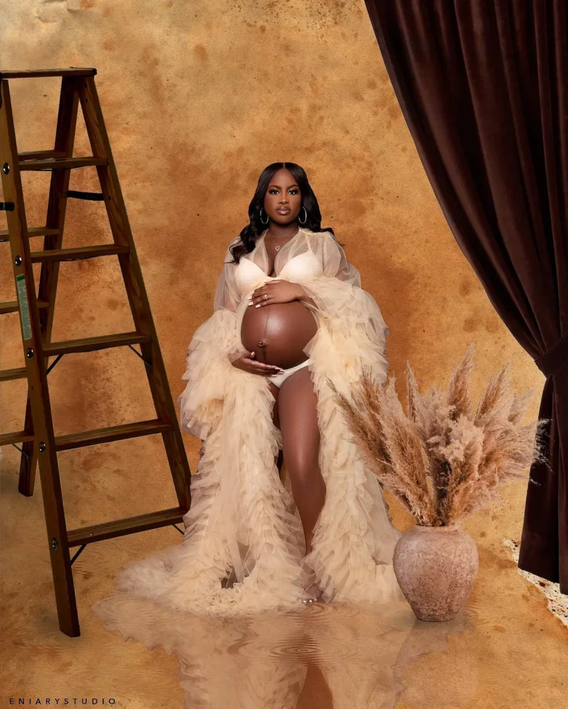 Editorial maternity portrait in a cream ruffle robe beside a wooden ladder set