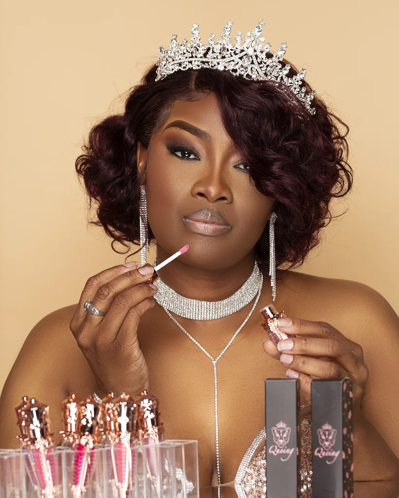 Beauty brand founder applying lip color beside a display of branded cosmetics