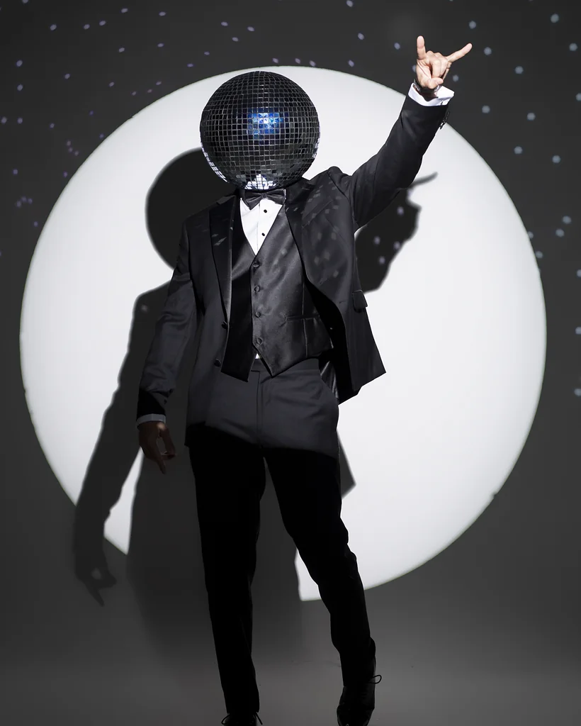 Creative entertainer in a tuxedo and mirrored disco helmet posed in dramatic spotlighting